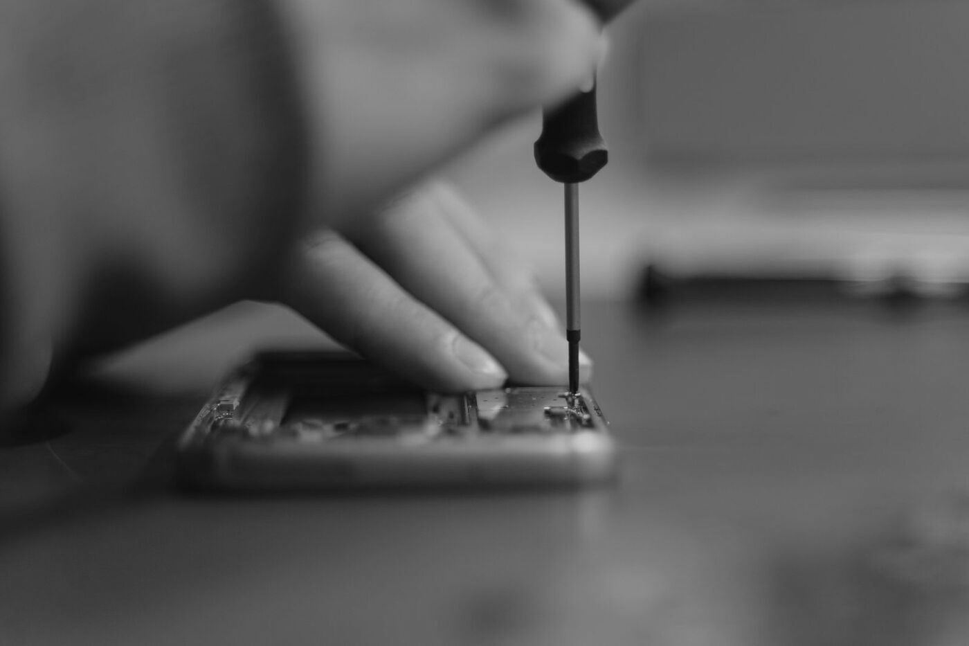 A hand with a screwdriver working on an opened circuit board