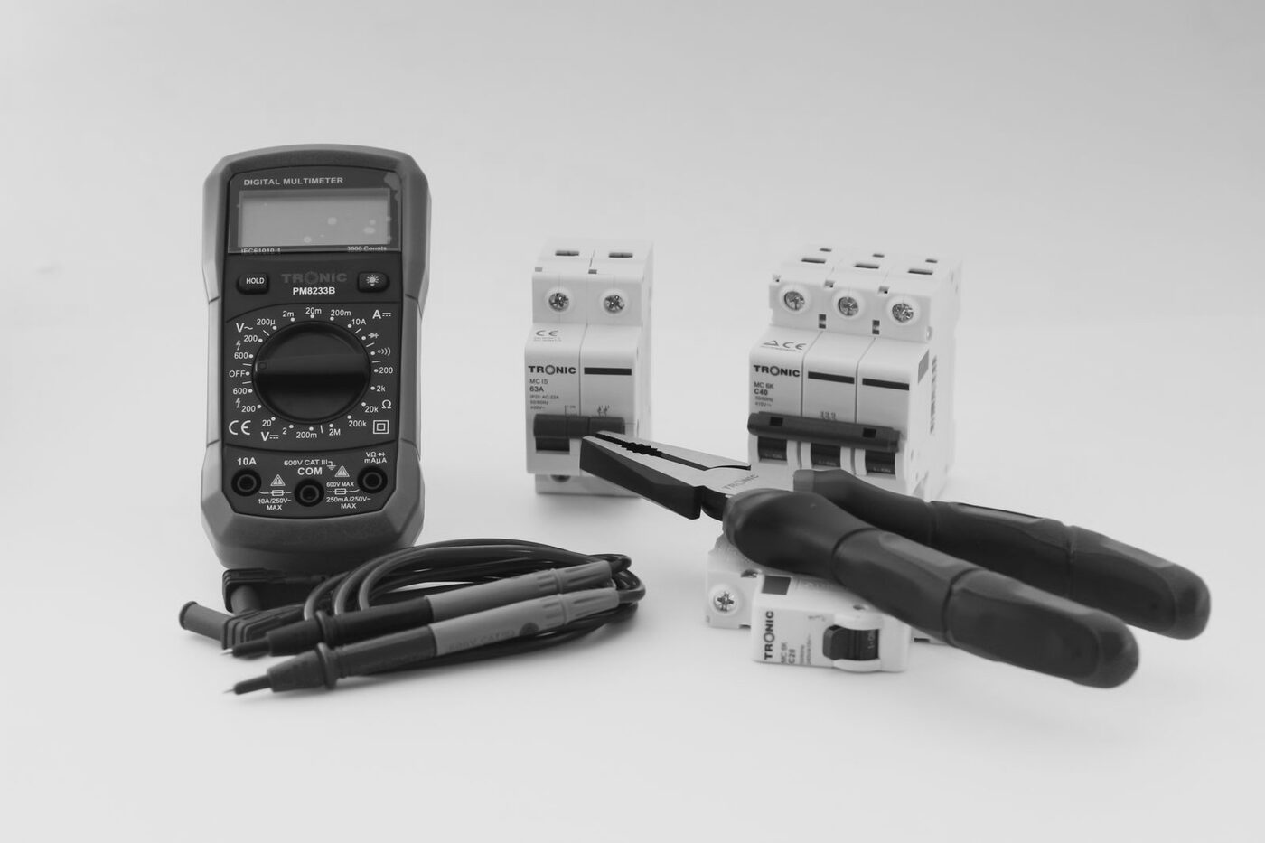Digital meter, circuit breakers, pliers and test leads on a light surface